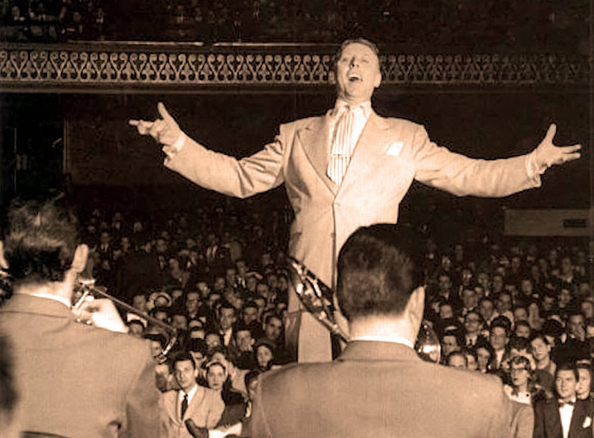 Vintage black and white photo of a male singer performing on stage with a large audience in the background, capturing classic music concert moments.