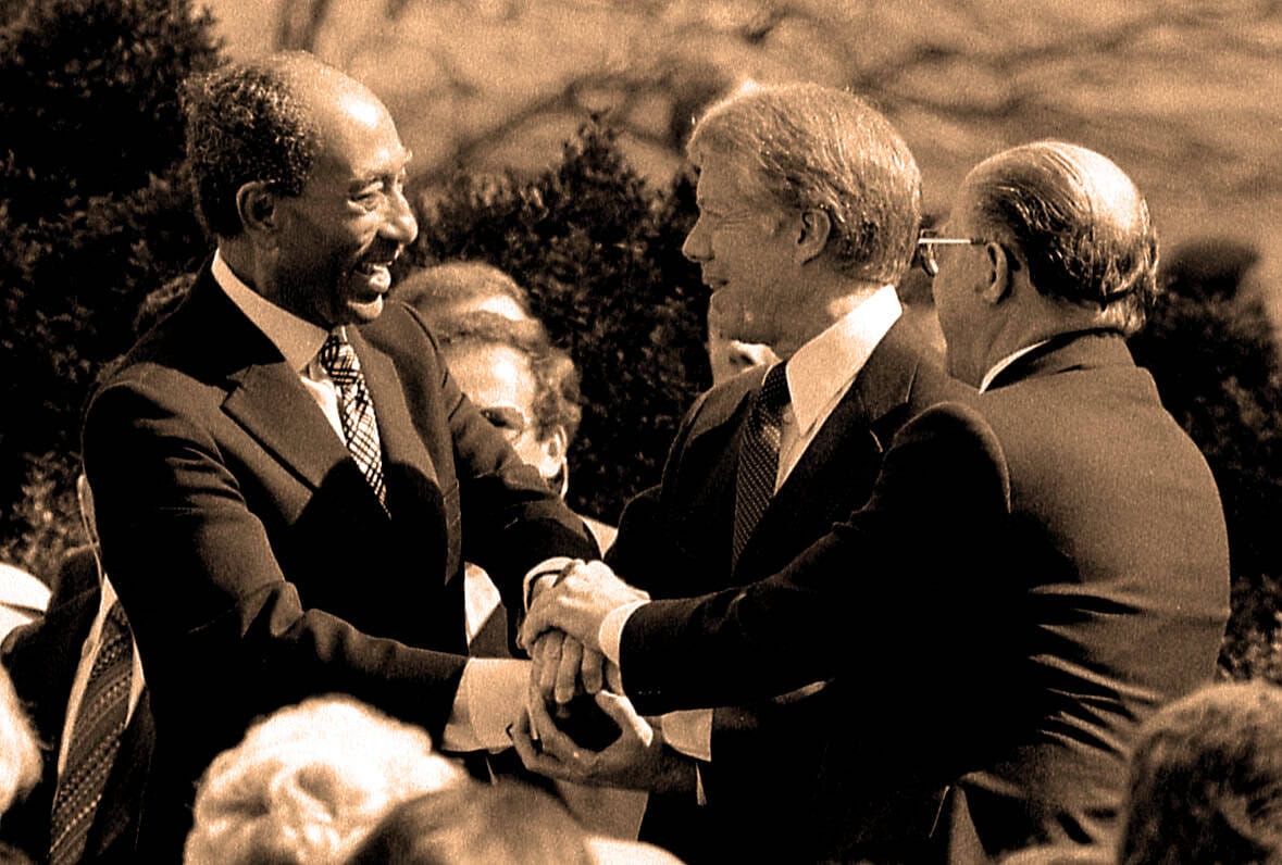 African American man shaking hands with a Caucasian man, both in formal suits, during a historic political event, symbolizing unity and leadership in a black-and-white photo.