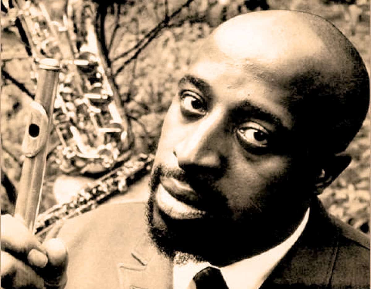 Black and white portrait of a man holding a flute, capturing a vintage music and news archive vibe, referencing historic recordings and cultural history.