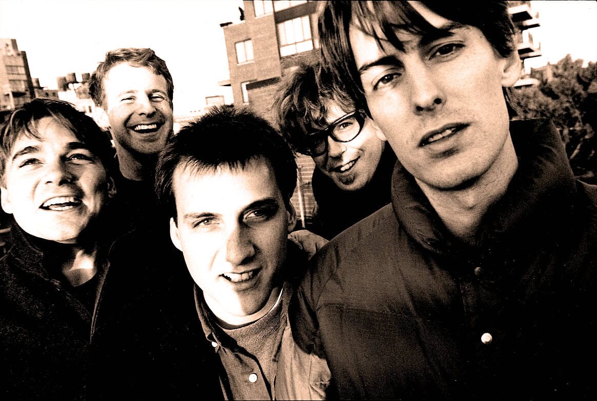 Young men smiling and laughing outdoors, rocks, historical buildings, casual clothing, band, friends, urban setting, black and white, energetic, candid shot, music and news archive, nostalgic mood, Past Daily archive, vibrant youth culture.