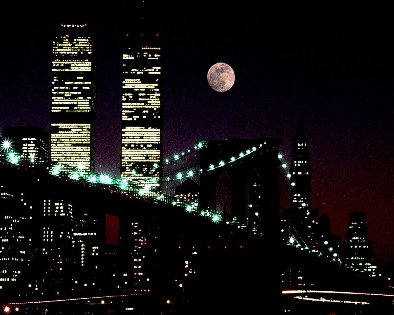 Brightly lit Brooklyn Bridge with NYC skyline at night, full moon in dark sky, iconic New York City architecture, city lights, urban night scene, popular travel destination, modern cityscape, nighttime city view, landmarks.