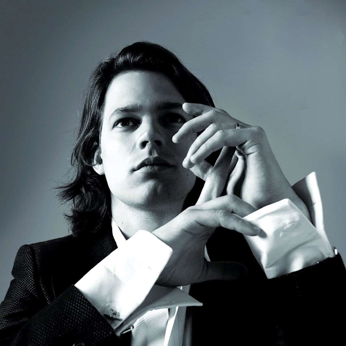 Elegant black and white portrait of a young man with long dark hair, dressed in a formal tuxedo, representing classic music and arts, suitable for a sound archive of news, history, and music.