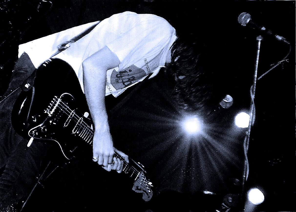 Guitarist performing live on stage at a music event, capturing a passionate moment in rock or alternative music, with dramatic lighting enhancing the concert atmosphere.