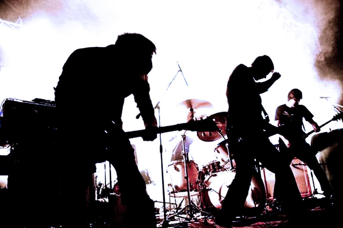 Silhouetted rock band performing live on stage with drums, guitar, and microphone, showcasing music history and concert energy at Past Daily, a sound archive for news, history, and music recordings.