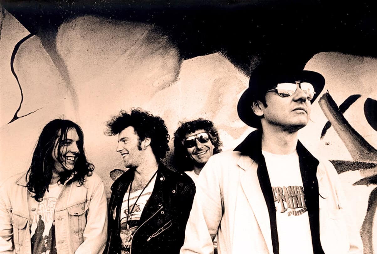 Vintage rock band photo, black and white image of musicians smiling and wearing sunglasses, graffiti background, music history, classic rock, nostalgia, legendary band, 80s music scene.