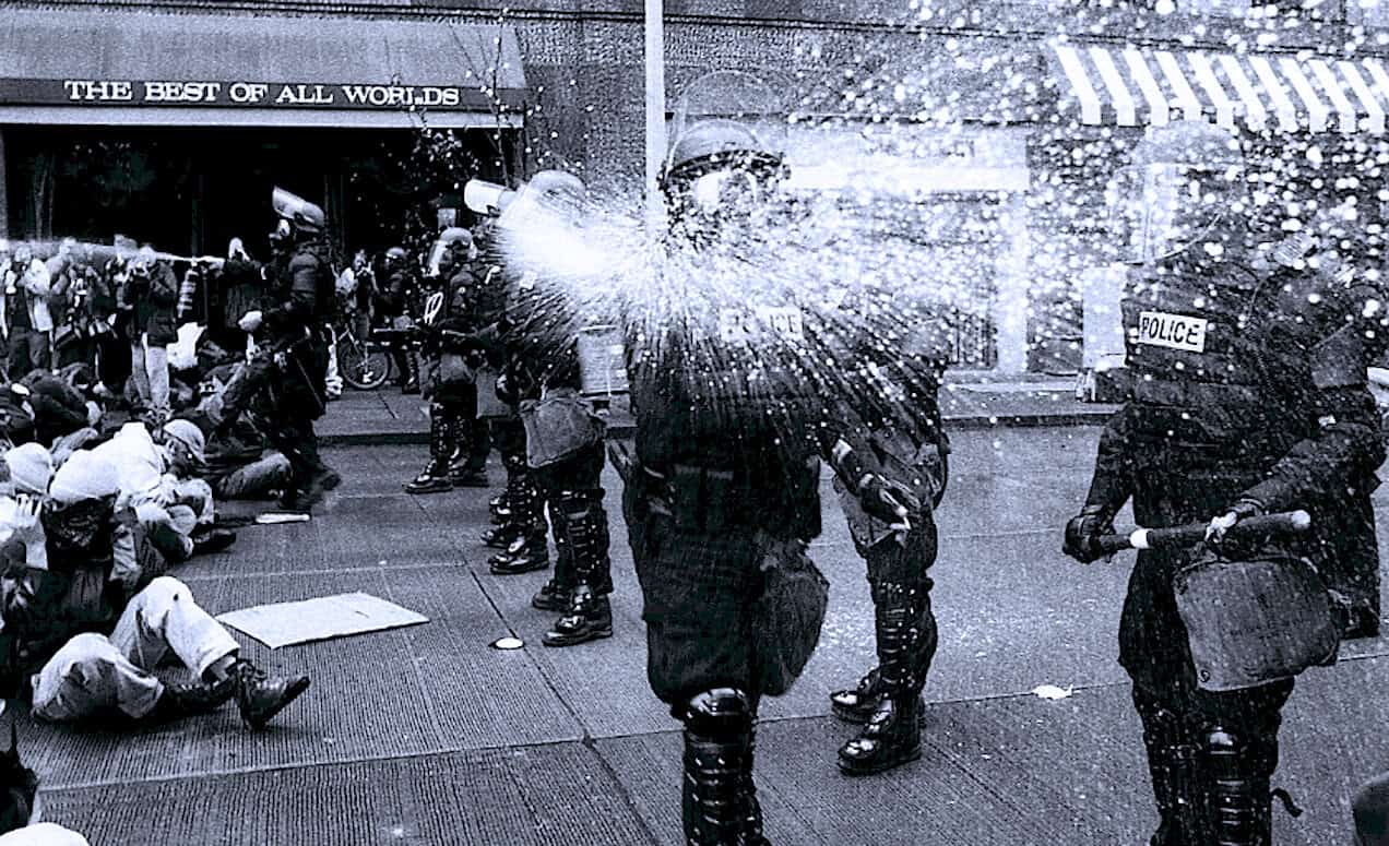 Police officers dispersing protestors with water cannons during a civil demonstration in an urban street scene.