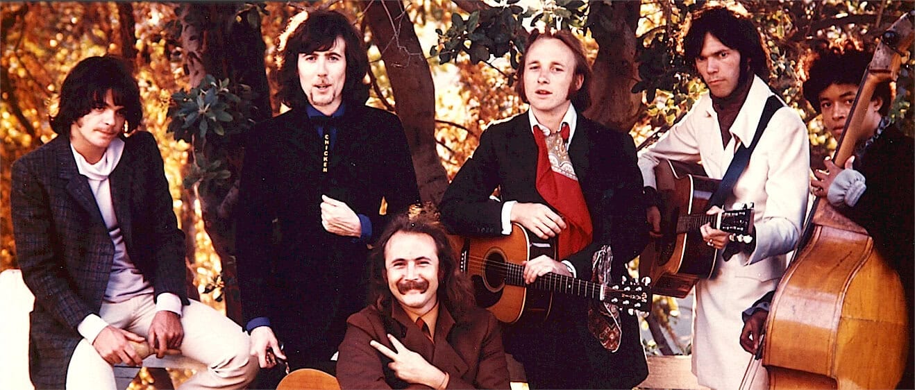 Rock band members playing guitars and bass outdoors during fall season, casual attire, music performance, vintage style, musical instruments, band photography, nostalgic music scene, classic rock band, music archive, music history, musical group, iconic band image, vintage music photo, past daily archive relevance.