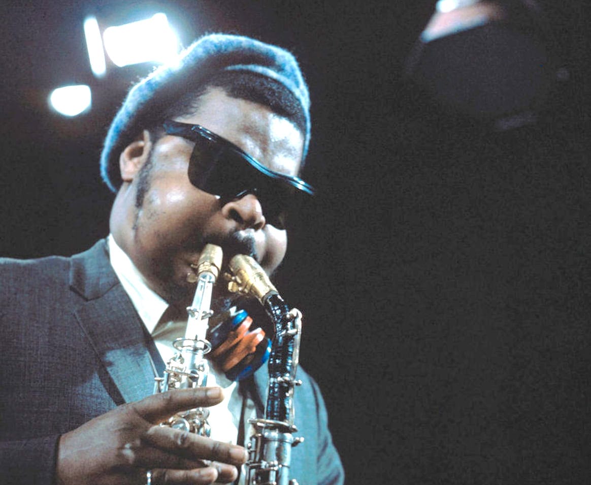 Jazz musician playing saxophone at a live music event, wearing sunglasses and a beanie, representing music and cultural history.