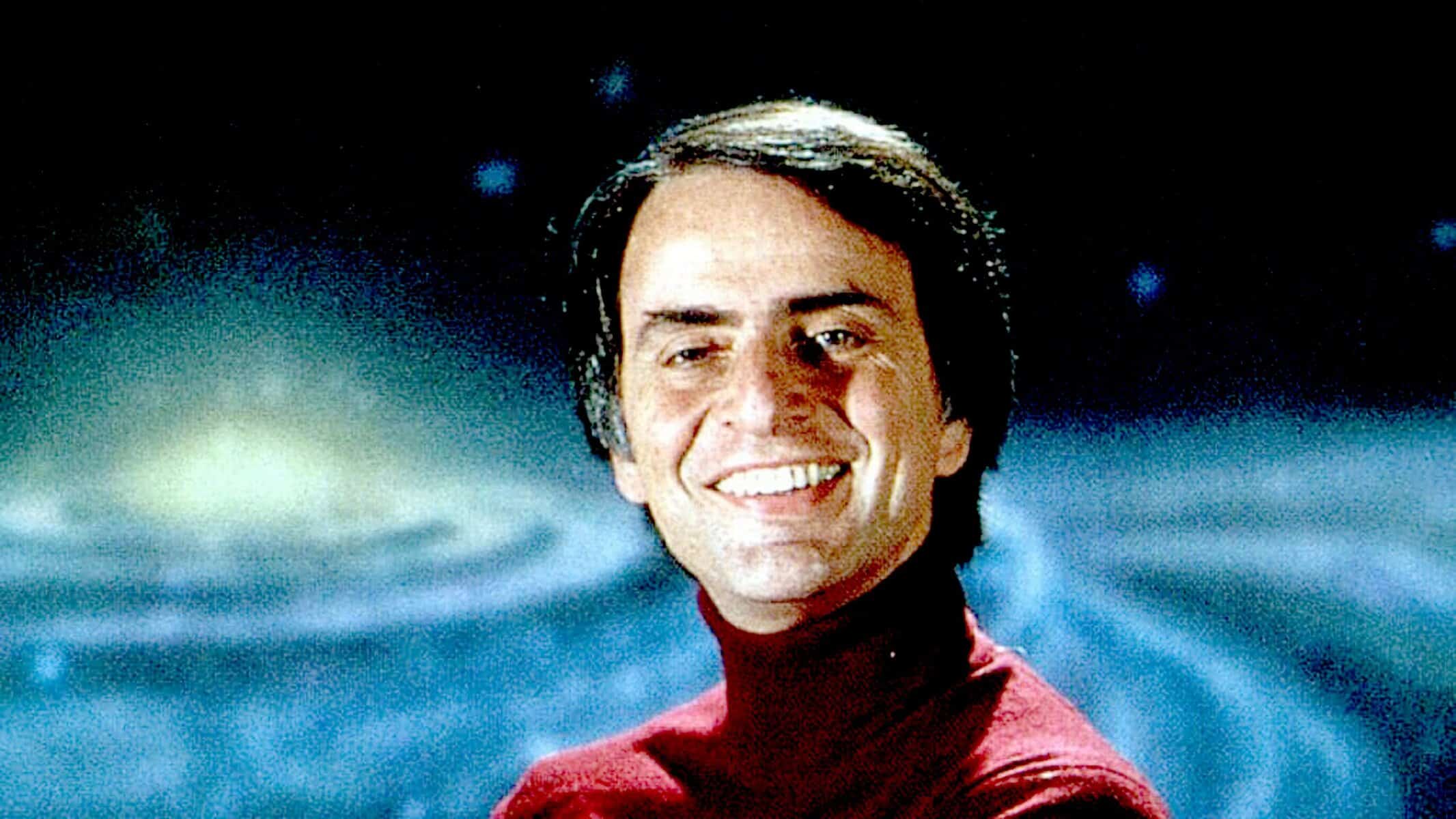 Photograph of a smiling man with dark hair wearing a red turtleneck, set against a cosmic background, representing nostalgia, history, and music archives.