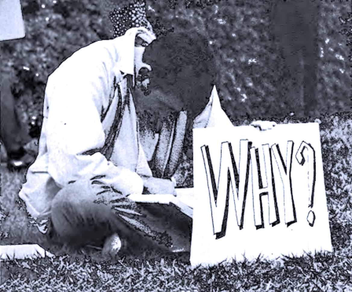 Homeless man sitting on grass holding a protest sign that says "WHY?" in large bold letters at a public demonstration or rally, black and white photo representing social issues and activism, Past Daily archive image.