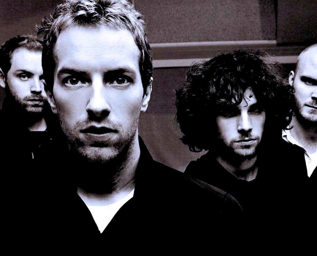 Young male band members in black attire with intense expressions, dark curly hair, and modern style, music band photo, promoting rock or alternative music scenes.