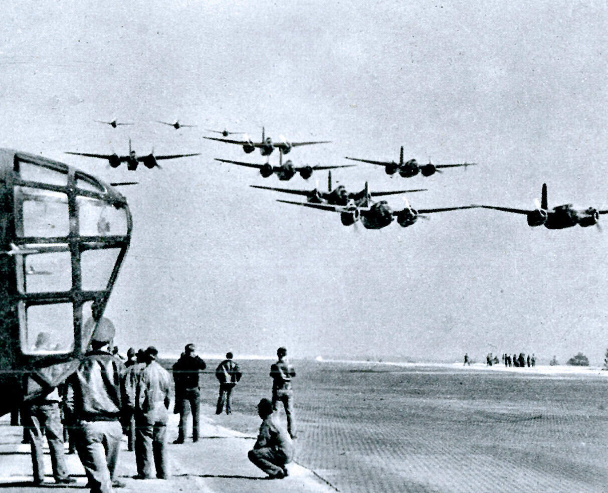 Formation of military aircraft flying in a V-formation during a historical air show or military exercise, with spectators watching on the ground.