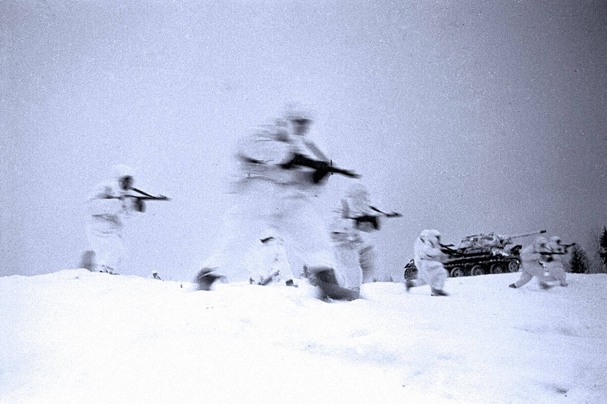 War soldiers in snow during military training or combat, with a tank in the background, black and white photo, historic Cold War or World War II era military scene, snow-covered landscape, pursuit of peace and war history, military archives, news, and history photography, from Past Daily sound archive of historical news and music.