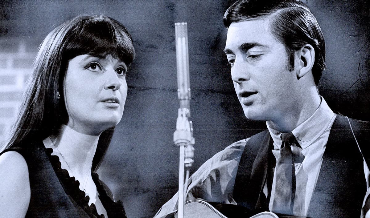 A black-and-white photo of two musicians, a woman and a man, performing with a microphone and guitar, showcasing classic music recording and broadcast elements; ideal for music audio archive and history.