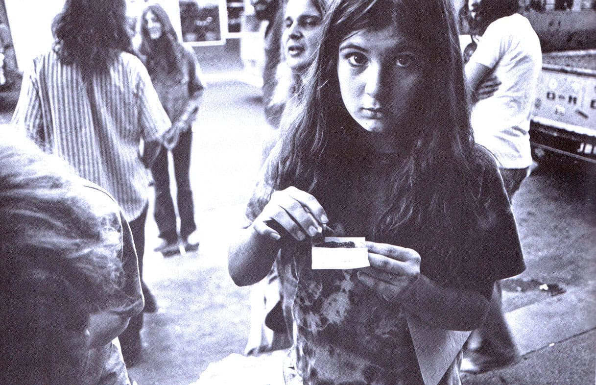Urban street scene with young woman holding a ticket, surrounded by pedestrians, capturing candid moments of daily life, nostalgia, and social interactions.