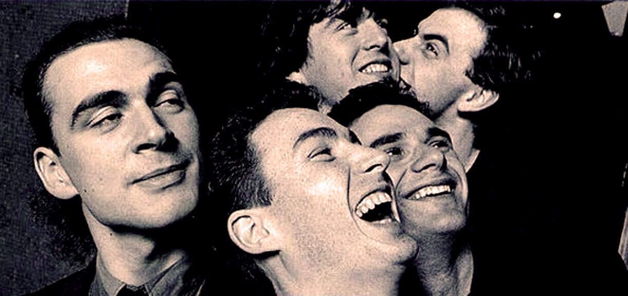 Vintage black and white photo of five men smiling and enjoying each other's company, capturing a moment of happiness, friendship, and camaraderie in a classic music and cultural setting.