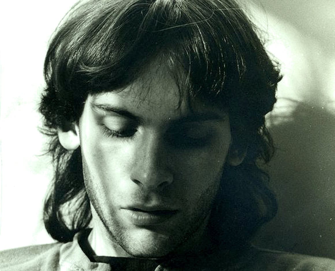 Soft focus portrait of a young man with long dark hair, closed eyes, and serene expression, capturing a nostalgic and timeless vibe related to historical news, music, and cultural archives.