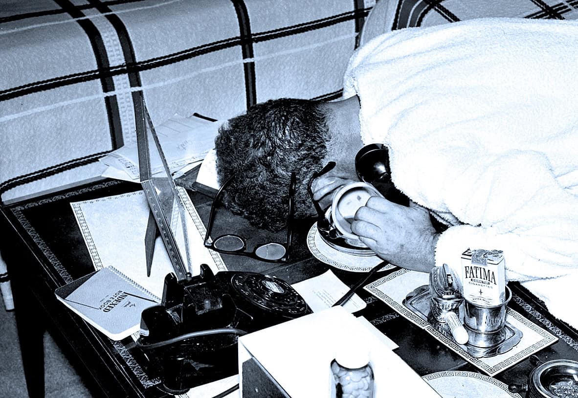 Vintage man with glasses using rotary phone at a cluttered desk, representing historic news, music, and sound archives.