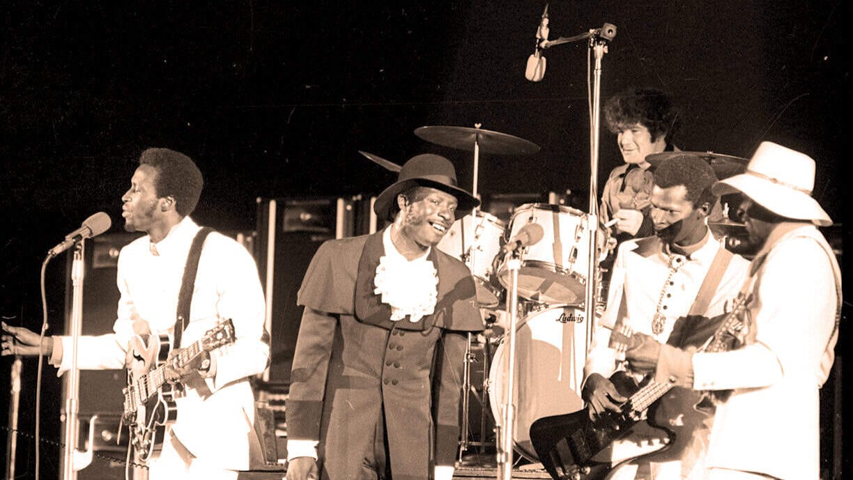 Historic black and white photo of The Mamas and the Papas performing on stage with musical instruments, capturing a moment of 1960s music history and folk-rock culture.