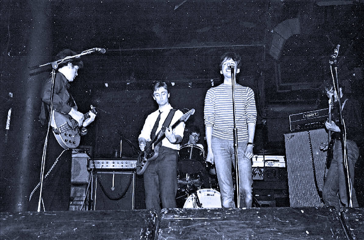 Vintage band performing live on stage with guitars and drums, capturing classic music culture and underground music scene, emphasizing historic live music performances and sound archive.