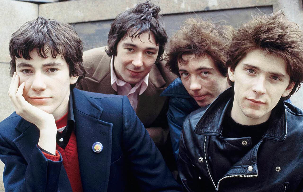 1970s British rock band members posing outdoors, casual fashion, classic rock music style, iconic music group, vintage band photo.