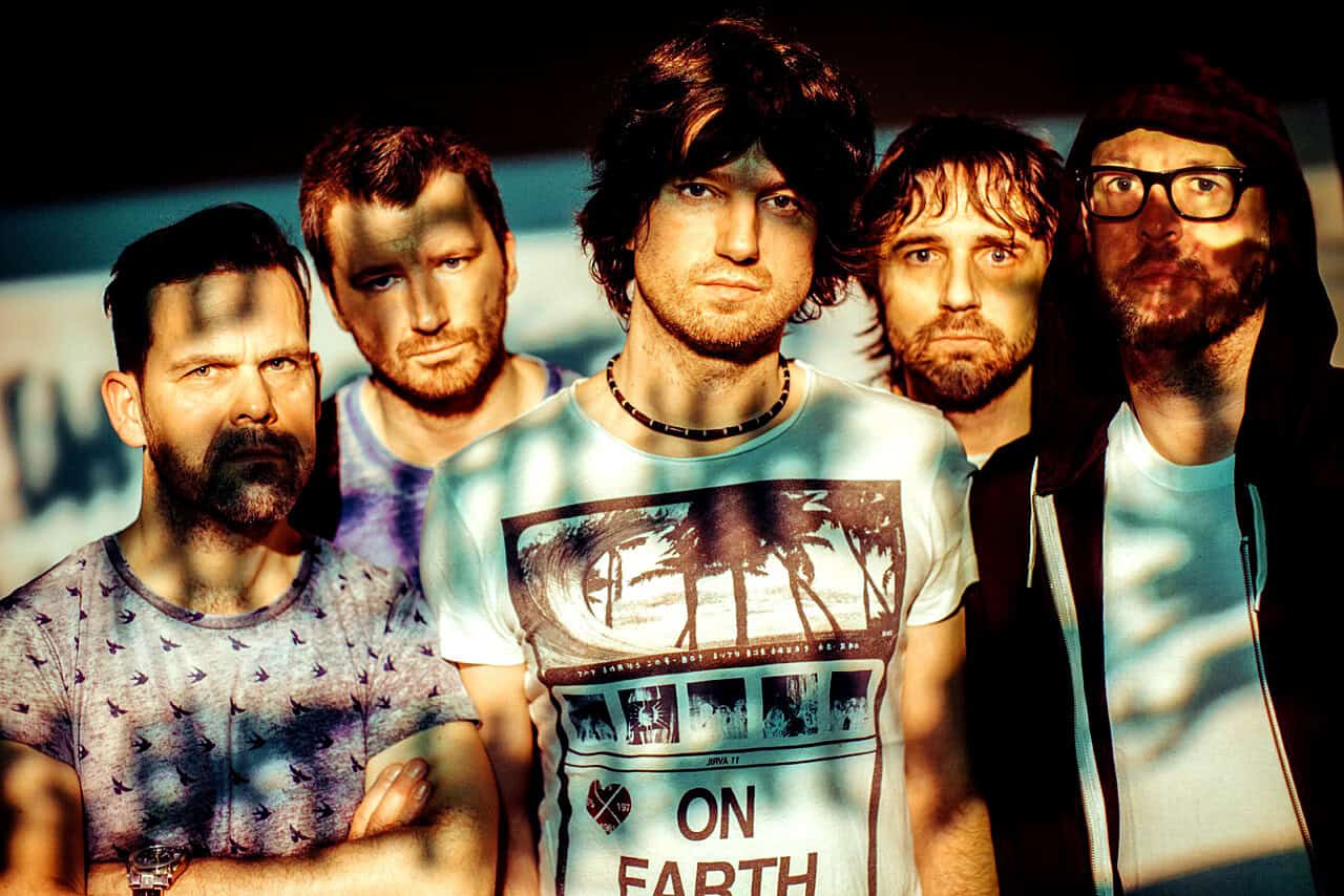 Small band of five young men posing outdoors with sunset lighting, casual clothing, and musical vibe, representing music history, bands, and American rock culture.