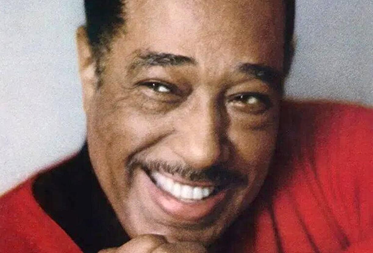Smiling man with mustache in red shirt, close-up portrait for sound archive of news, history, and music, Past Daily logo in background.