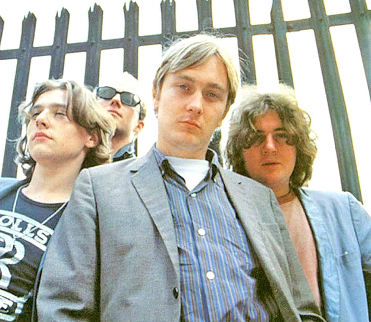 Vintage punk rock band photo with rebellious style and attitude, featuring iconic members outside a metal fence, capturing the essence of 1970s music history and culture.