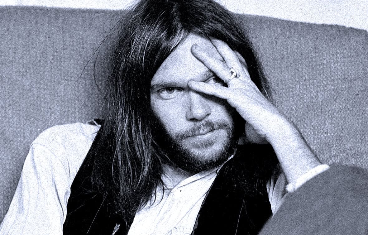 Young man with long hair and beard, covering one eye with his hand, in black and white photo.