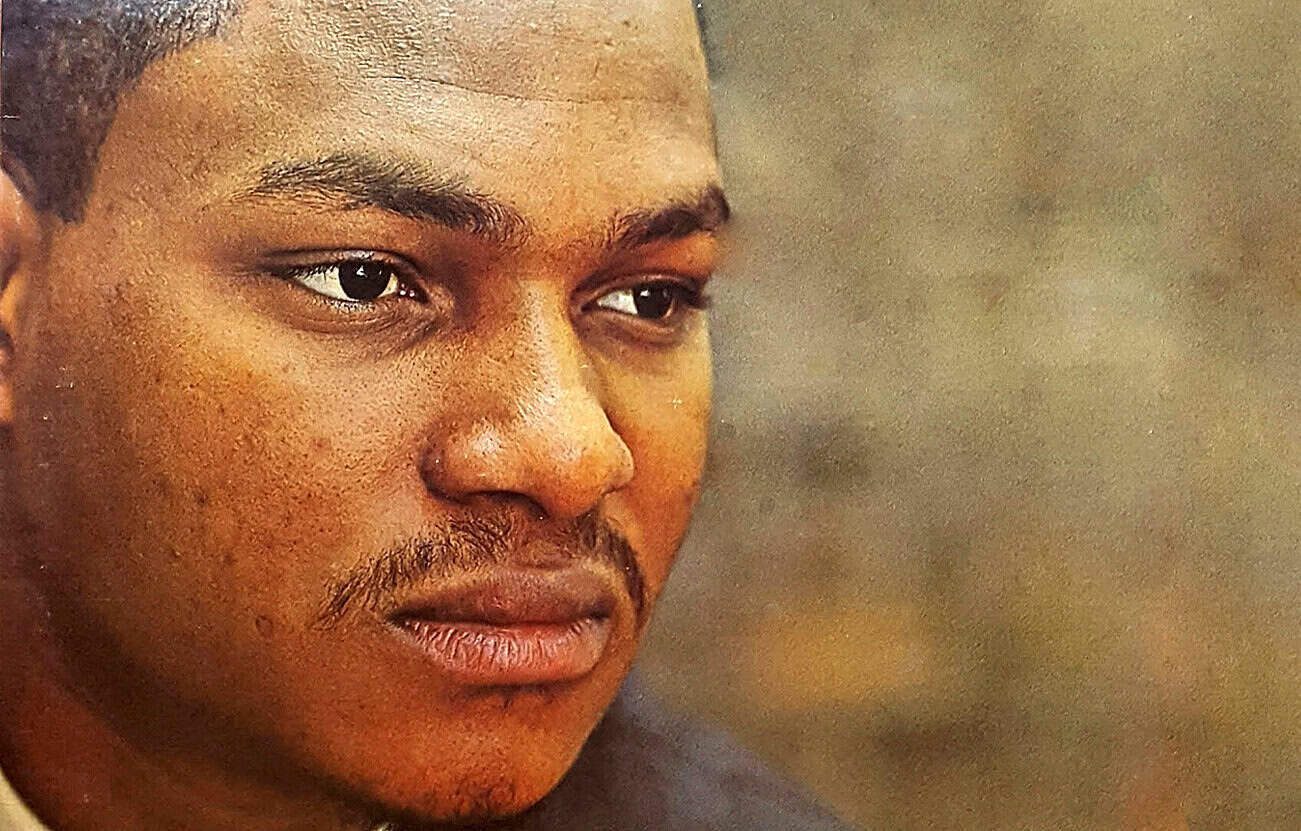 Close-up of a young African American man with a serious expression, emphasizing the importance of historical news archives and music recordings.