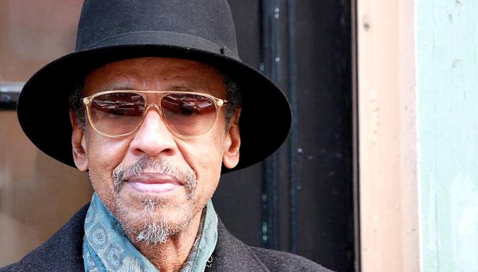 Senior man with sunglasses and fedora, enjoying a nostalgic moment amidst classic music and news history.