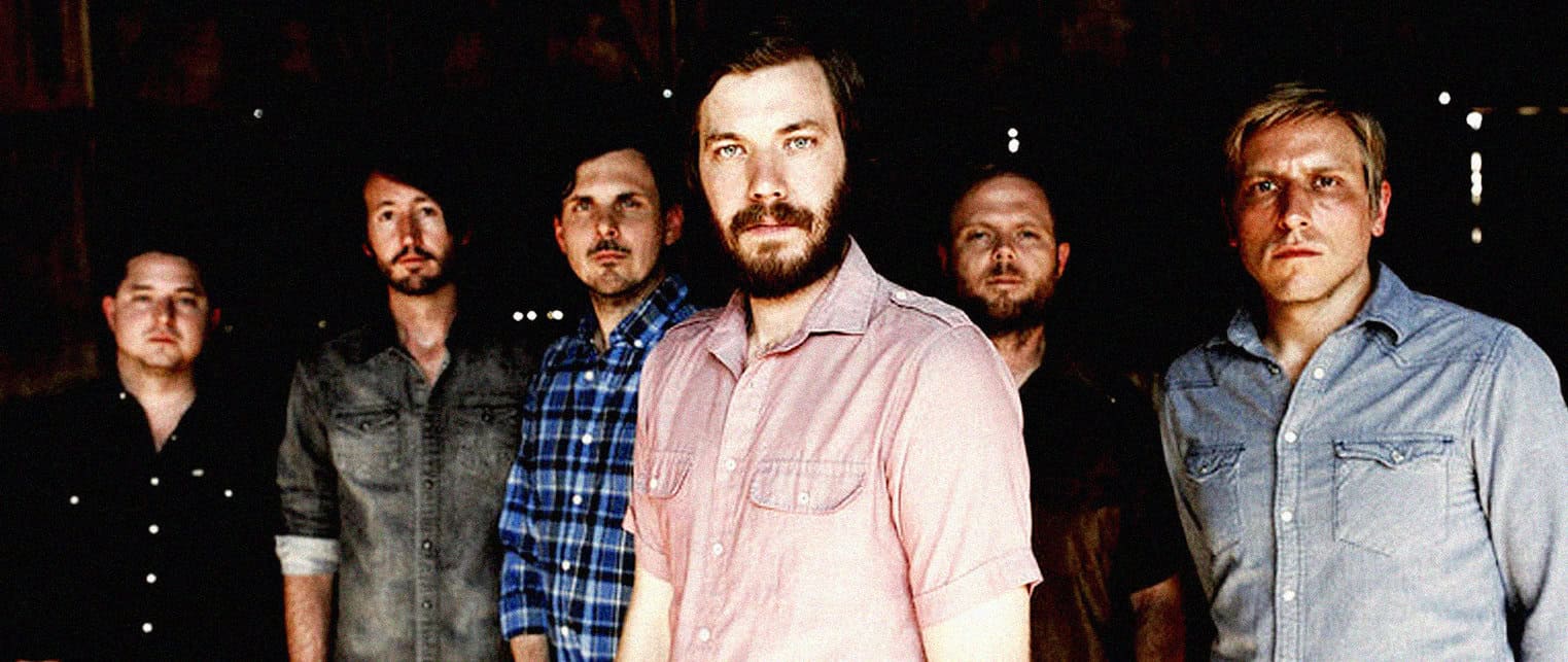 Vintage rock band members standing in a dimly lit music venue, showcasing iconic music history and live performance atmosphere.