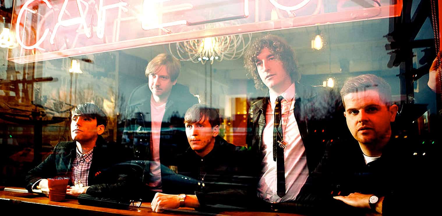 Vintage band members sitting inside a cafe, capturing the essence of music history and retro culture, with a neon sign visible through the window.