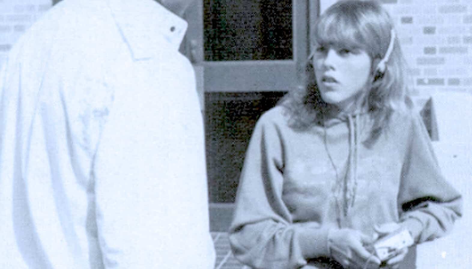 Muted black and white image of a young woman with headphones, talking to a person in a white shirt, capturing a moment of conversation related to news, history, and music archives.