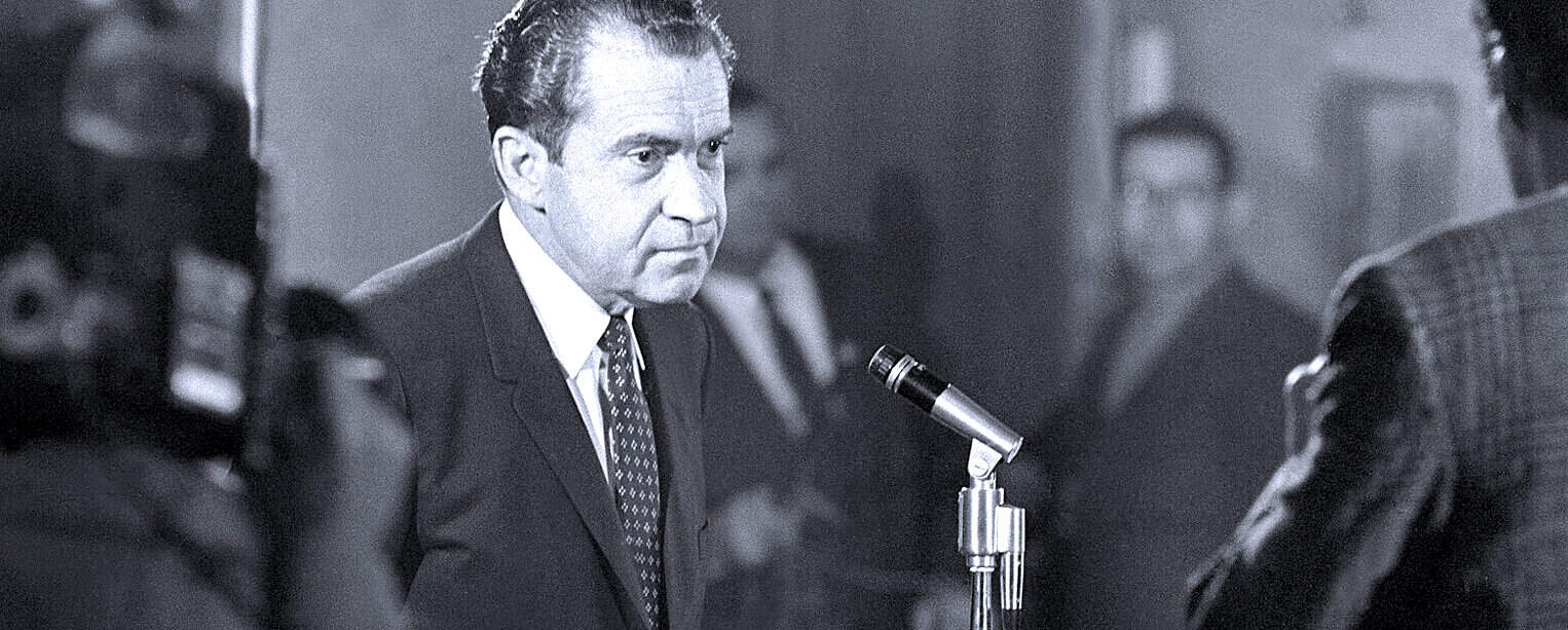 History of TV broadcast news interview with a journalist in a dark suit and tie at a formal press conference or media event, emphasizing news archive, historical journalism, and media recordings.