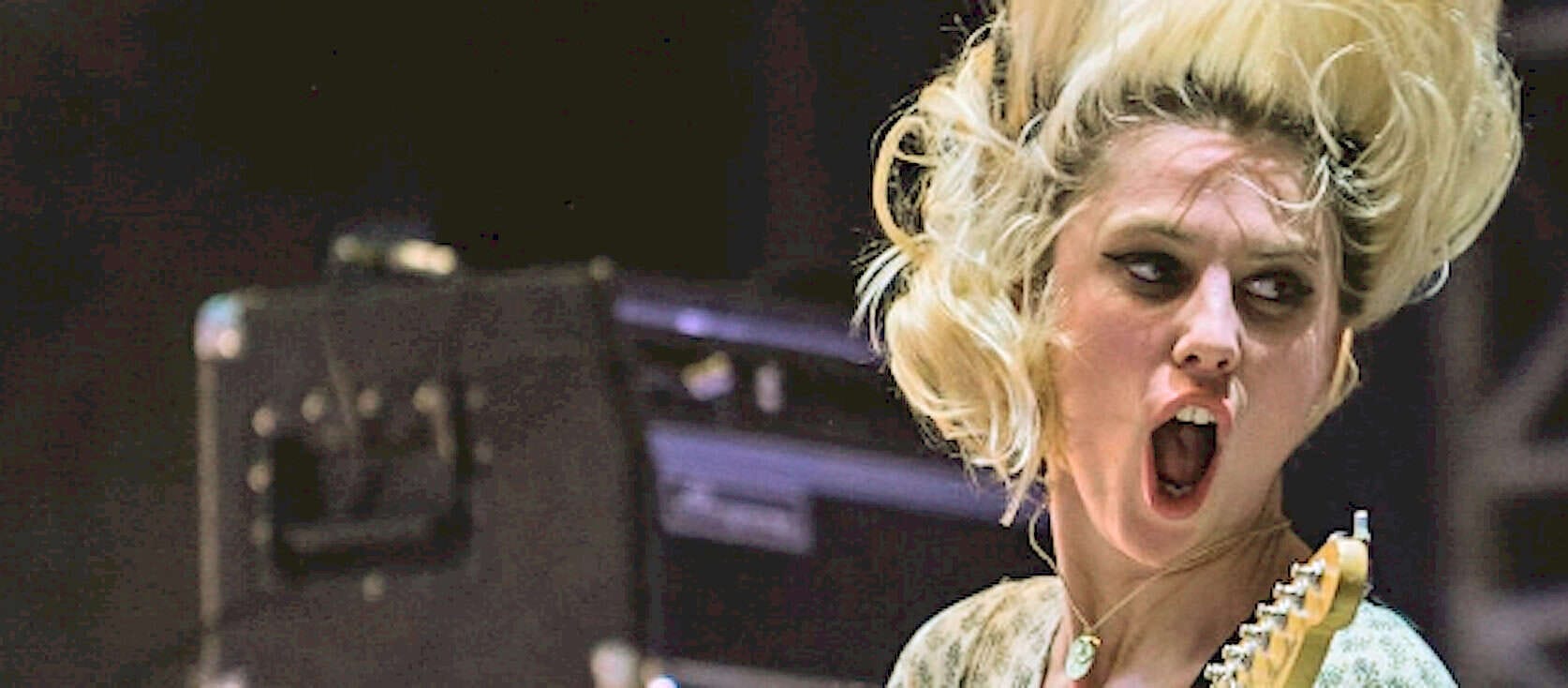 Woman performing with electric guitar at concert, rock music, music history, vintage style, energetic performance, music archive, news and culture, historical music footage, classic rock imagery, past daily sound archive relevance.