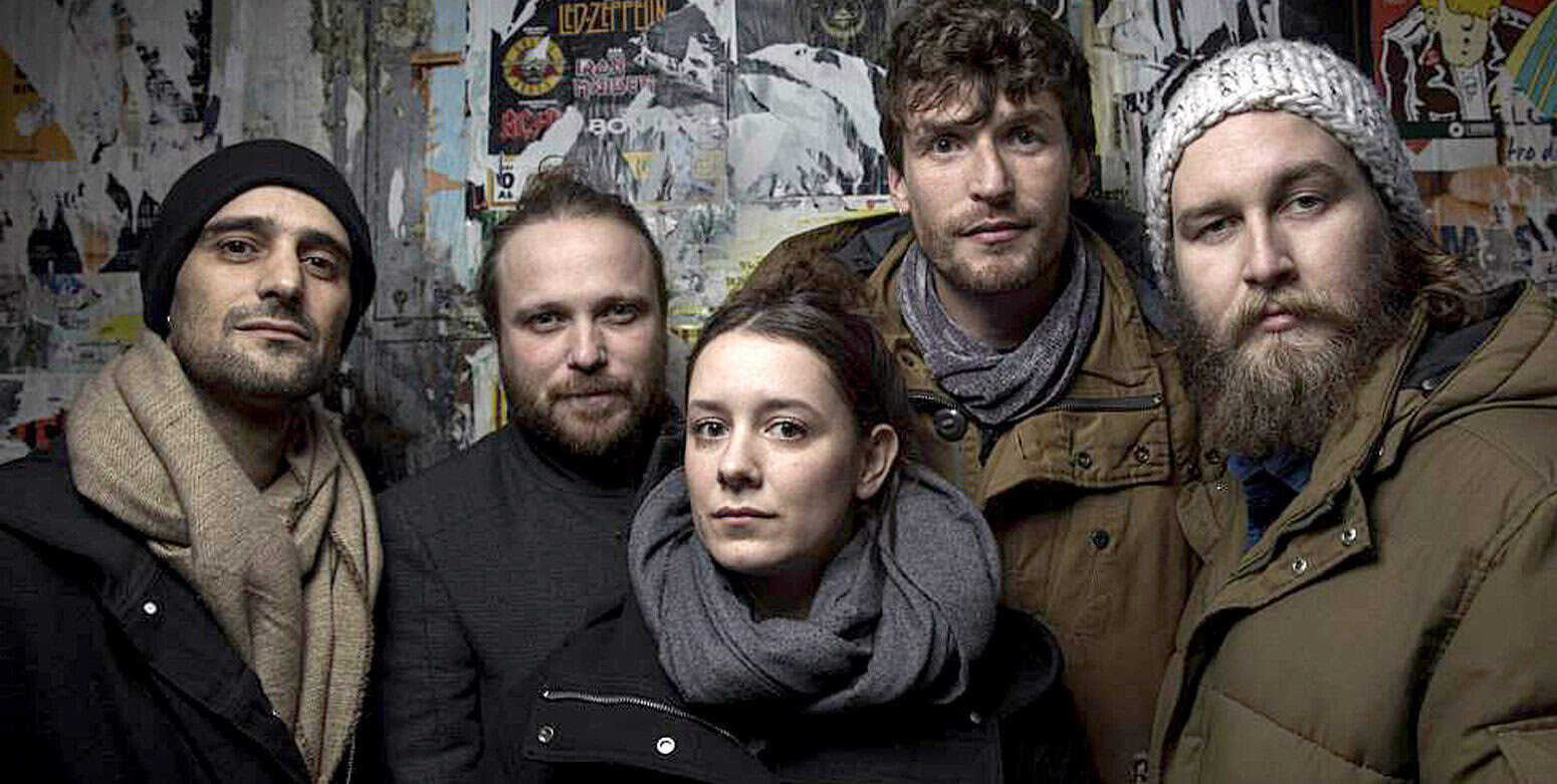 Beard man with gray beanie and bandana, group of young adults in casual jackets, urban background with posters, modern music band photos, diverse young musicians, indie band portrait, energetic music scene, music group photo, adolescents with style, contemporary music artists.