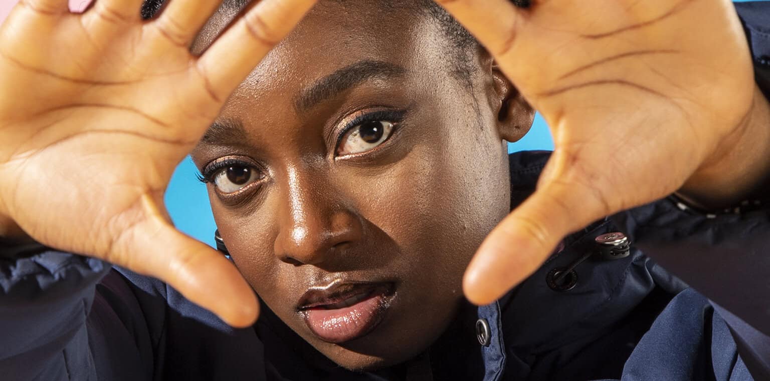 Vibrant portrait of an African American woman making a heart shape with her hands, emphasizing diversity, self-love, and empowerment; perfect for music, news, and history archive content.