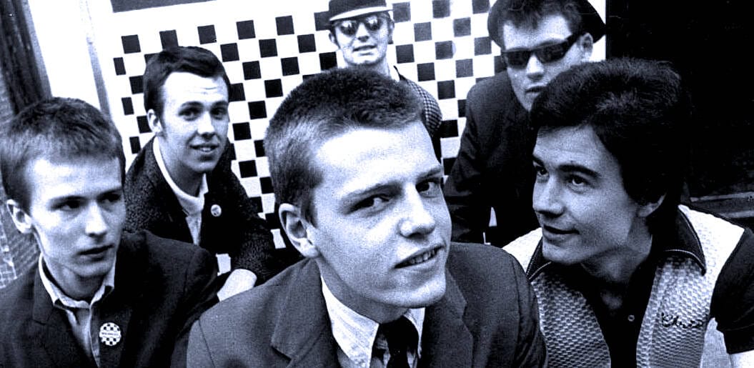 Young men in a band or musical group, dressed in suits, with some wearing sunglasses, in a black and white photo.