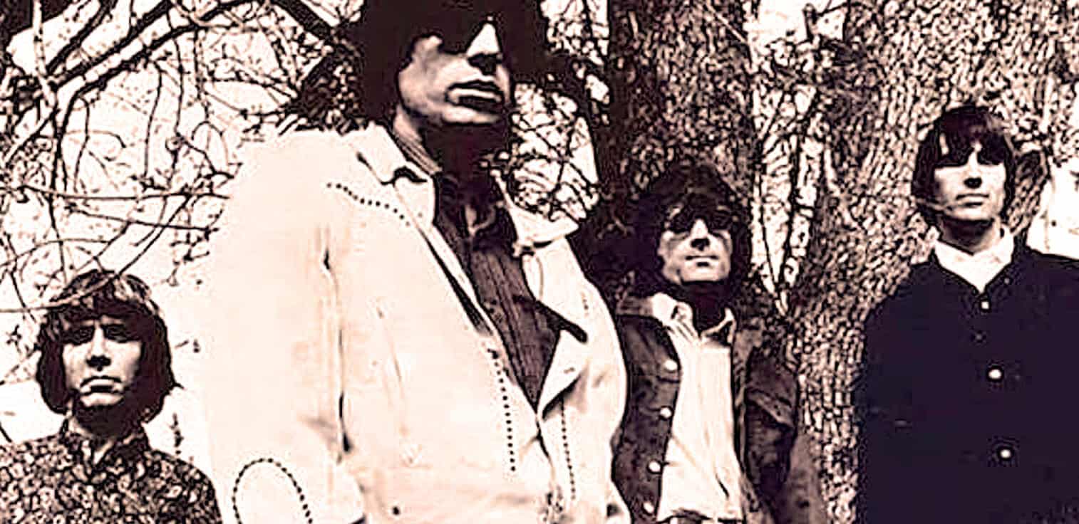 Vintage rock band photo from the 1960s, featuring four members with dark clothing and sunglasses, standing outdoors against a tree. Iconic imagery of classic rock history and music archives.