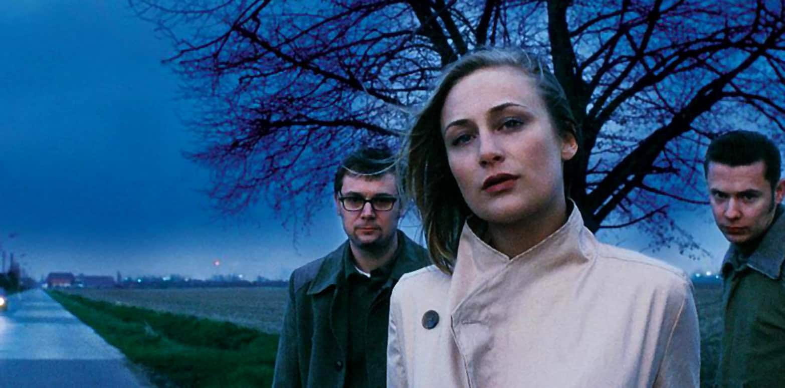 Moody women and men standing outdoors during dusk, atmospheric scene capturing news, history, and music archives, reflective of past daily audio recordings, with somber sky and leafless trees in background.