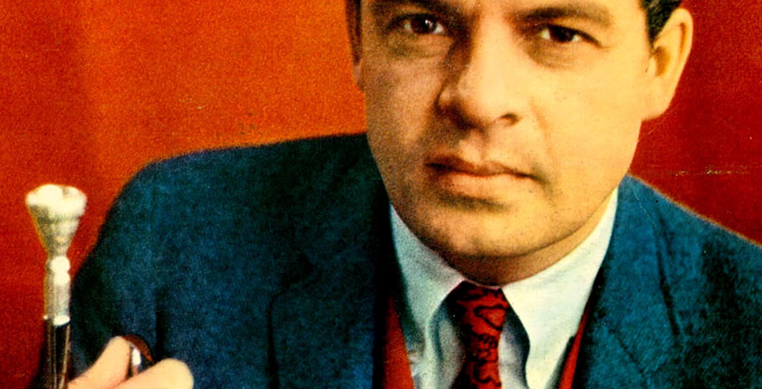 Close-up of a man in a suit holding a microphone, vintage style.