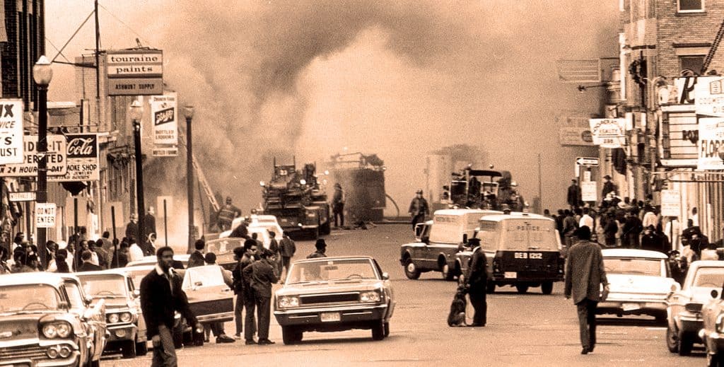 Explosive fire and smoke on a busy city street, vintage black-and-white photo capturing chaos with pedestrians, cars, and emergency response, illustrating historic urban disasters and news coverage.