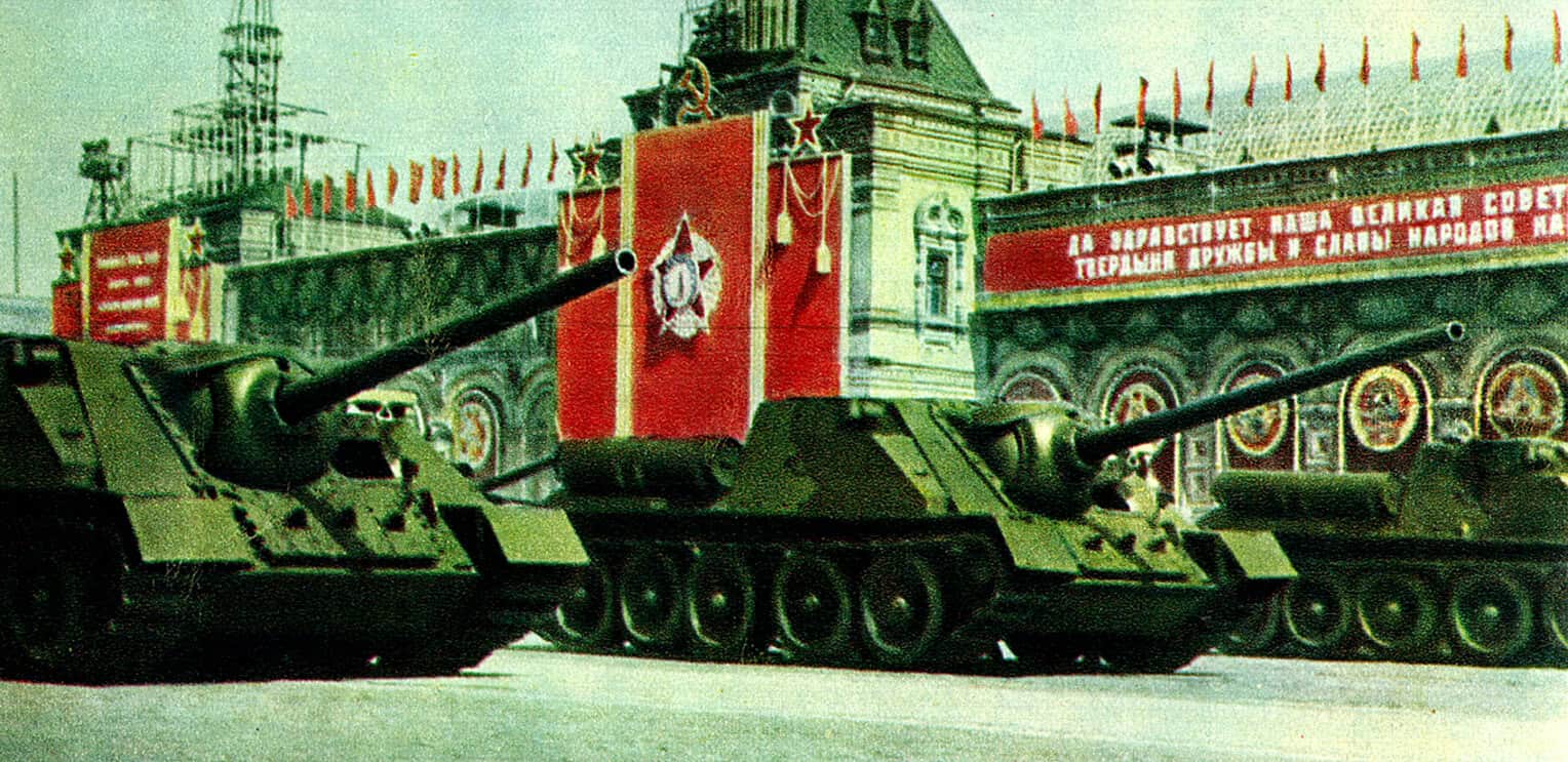 Tanks with Soviet Union flags and banners celebrating communism in Red Square during a historic Soviet parade.