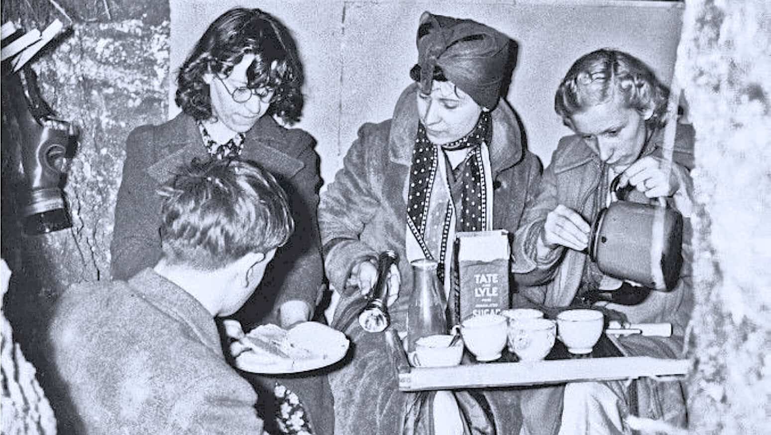 Historical photo of women and children sharing a meal and tea, vintage setting, nostalgic history, old-time food and social gathering, documentary image of daily life in the past.