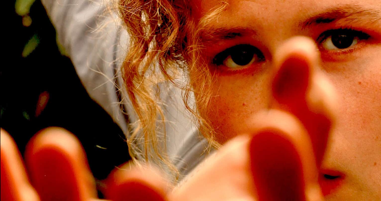 Close-up of a young girl with red curly hair and freckles, looking into the camera with an intense and curious expression. Perfect for themes related to childhood, nature, and media archives like Past Daily.