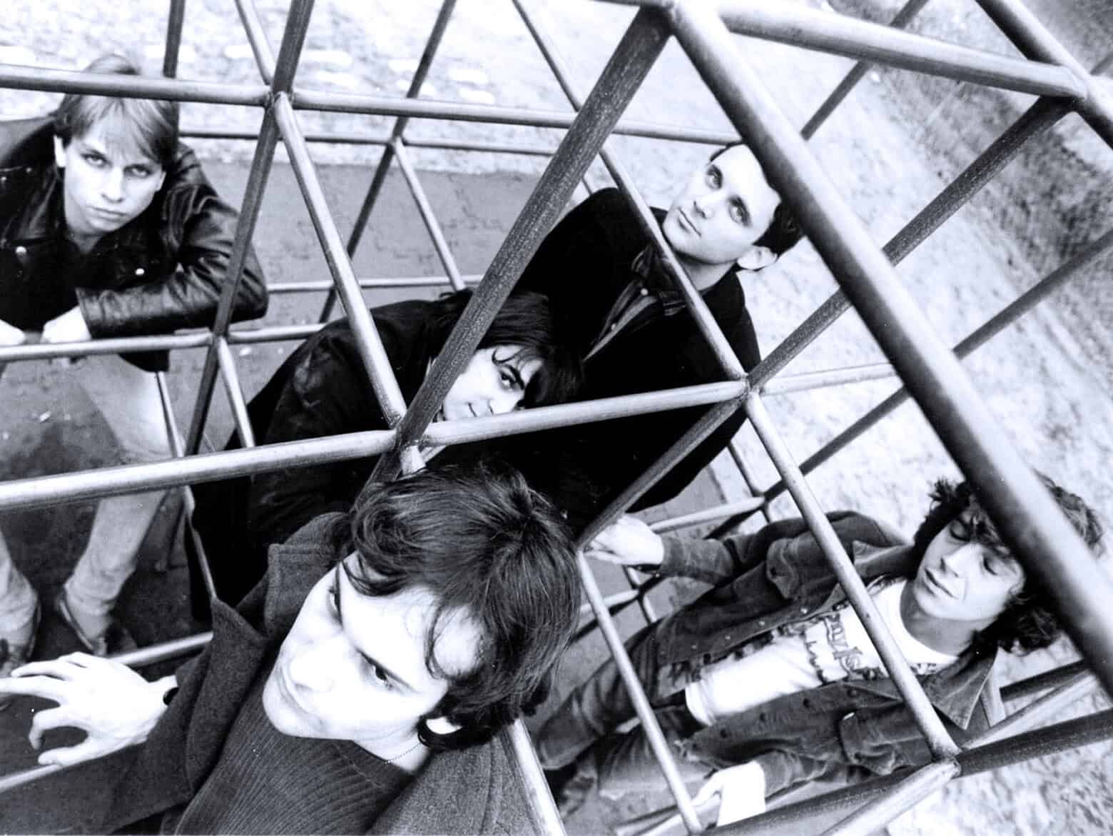 A black and white image of a punk rock band sitting inside a metal jungle gym structure, capturing their edgy style with bold expressions and rebellious attitude.