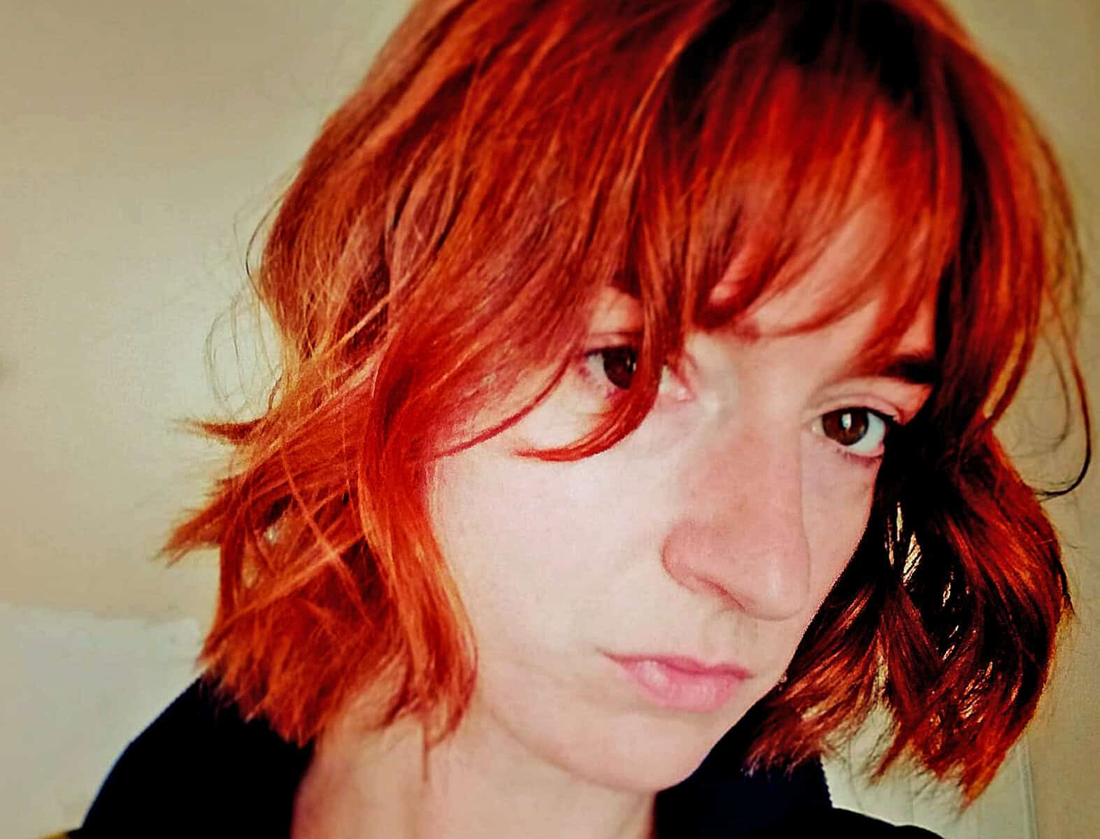 Vibrant red-haired woman with wavy hair, natural makeup, and a contemplative expression, representing the diverse history of news, music, and cultural archives on Past Daily.