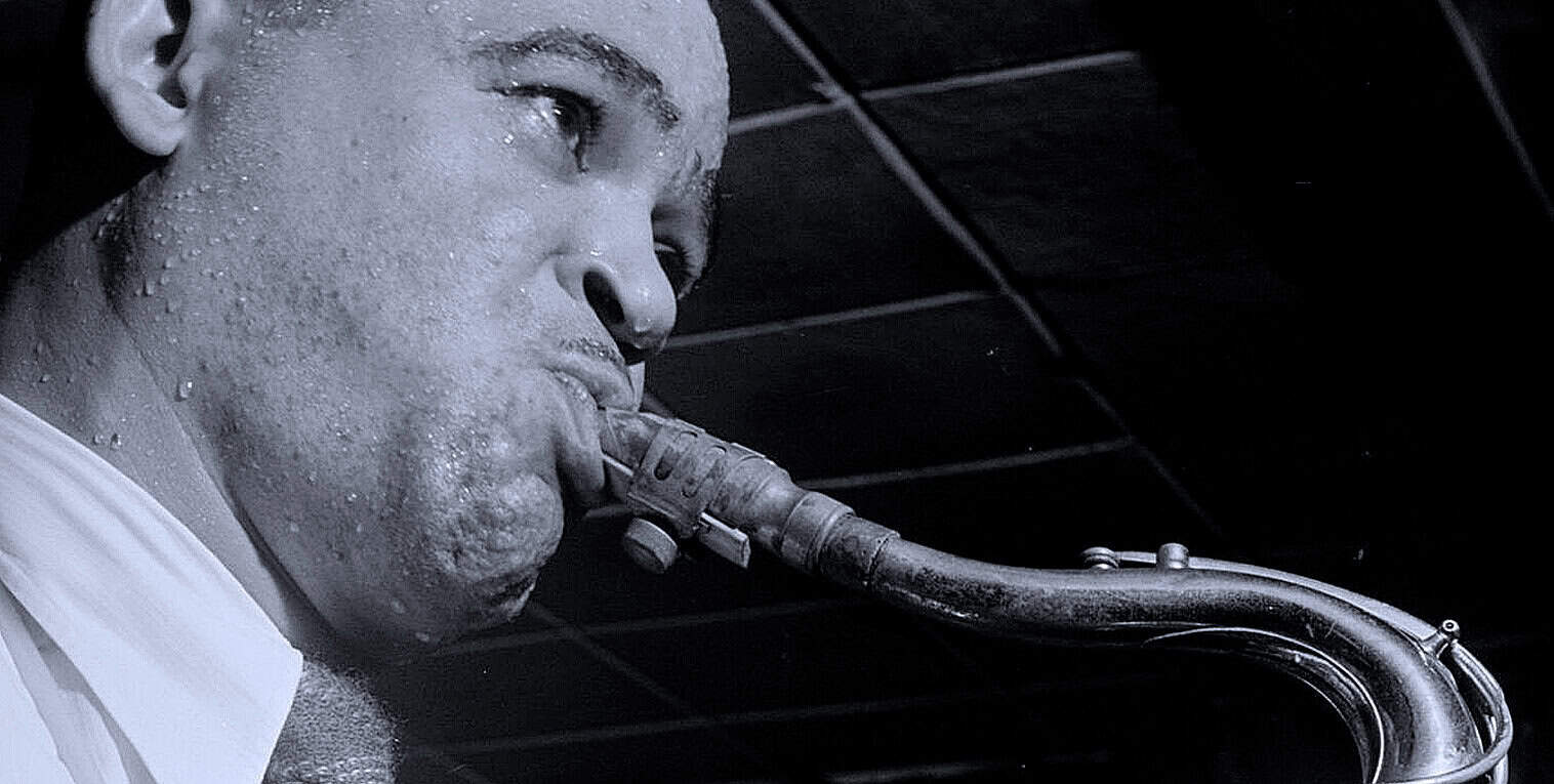 Close-up of a jazz saxophonist playing his instrument, with water droplets on his face, capturing the emotion and passion of live music performance.