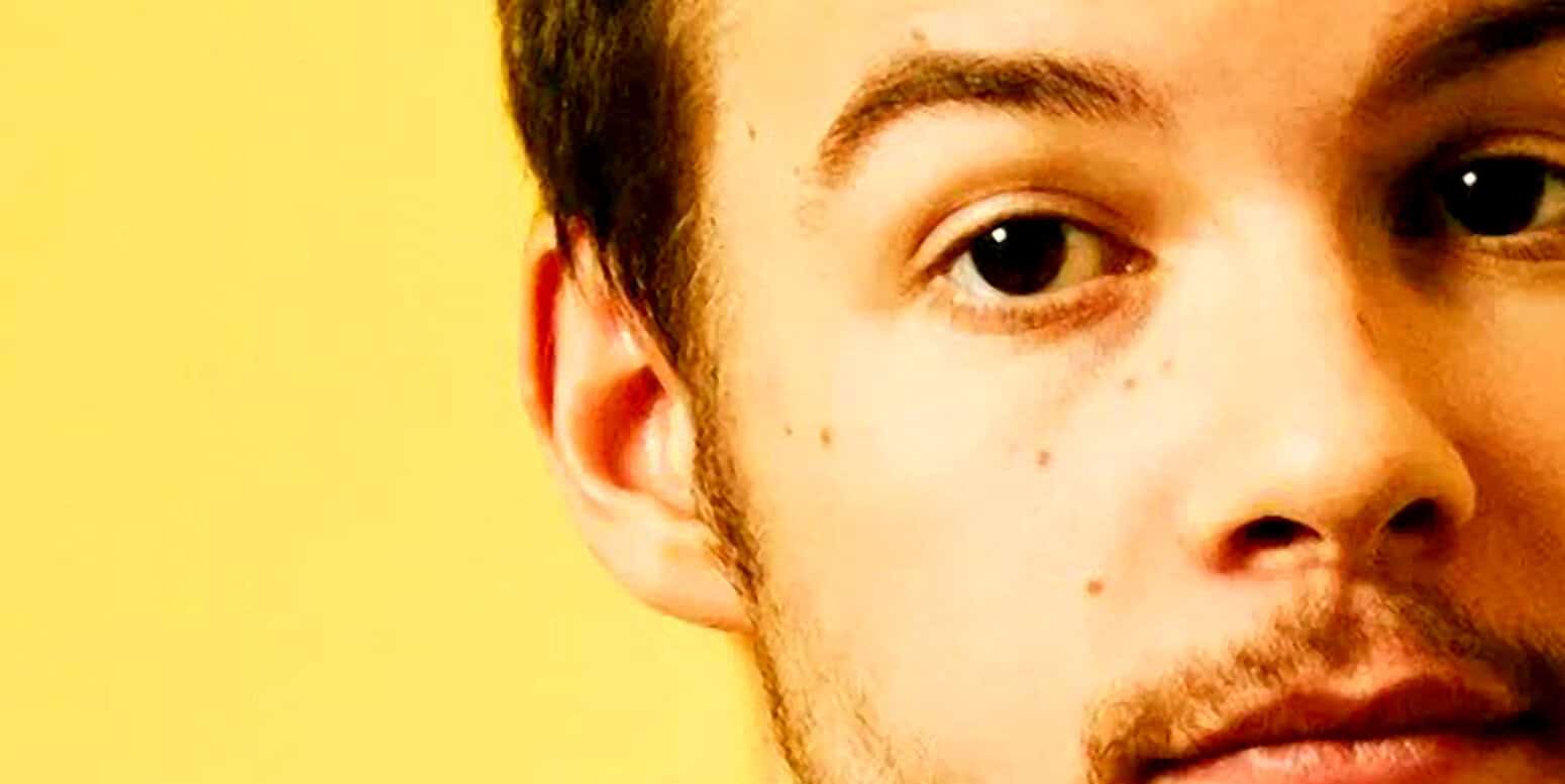 Close-up of a young man's face, showing clear skin, eye, and nose, with a yellow background, emphasizing themes of human expression, personality, and portrait photography.